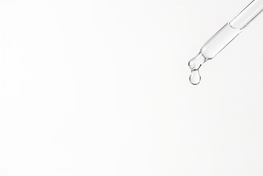 A pipette holds a drop of water that is just about to fall. The background is completely blank and white. There is lots of empty area for text or design