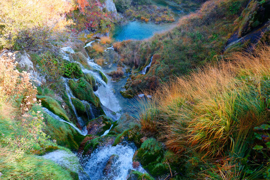 Terraced turquoise lakes cascade over tufa barriers surrounded by vibrant autumn foliage in Plitvice Lakes National Park, Croatia.