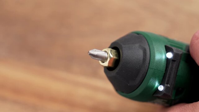 Green cordless screwdriver with illuminated LED light ring and crosshead bit spinning on wooden background. First launch or test of electric hand tool for DIY home improvement