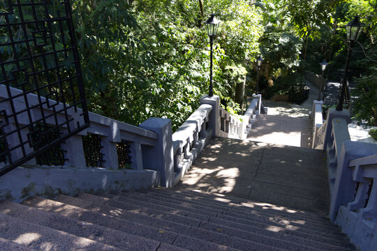 High-angle view of concrete stairs with ornate grey balustrades descending. Classic black street lamps illuminate the path.