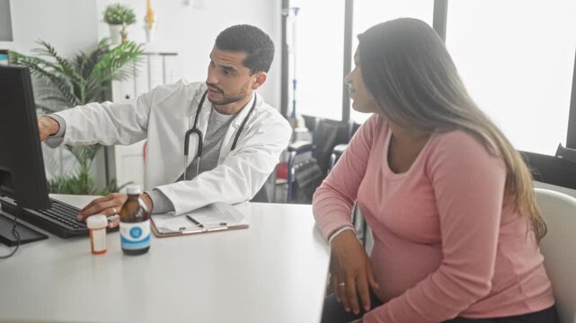 Pregnant woman touches belly while doctor in white coat points to computer screen and types during consultation in a clinic building; reassurance trust care.