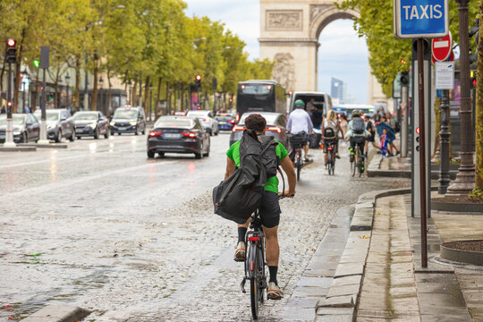 Urban bicycle commuters riding on a wet paved lane next to vehicle traffic with the iconic Arc de Triomphe in Paris France