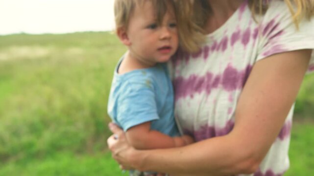 Mother carrying her toddler while walking through a lush green field on a summer day