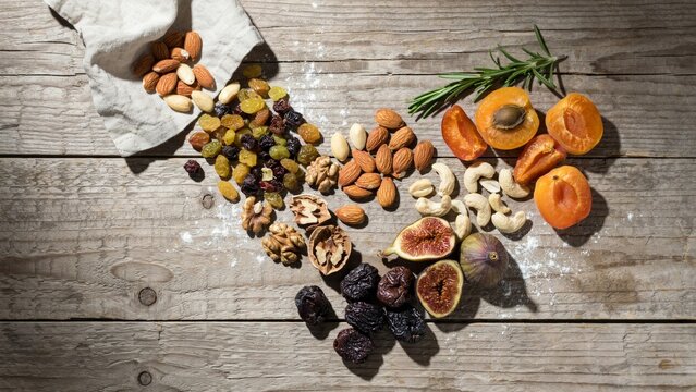 Assorted healthy dried fruits nuts and fresh apricots arranged on rustic wooden table with rosemary herb for nutritious snack photography