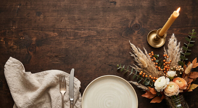 Elegant table setting with plate cutlery candle and floral arrangement for autumn dinner.