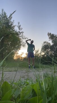 young person transitions from forward bend to upright resting stance on dirt path at sunset, low ground-level viewpoint, warm backlight, long shadows, silhouette