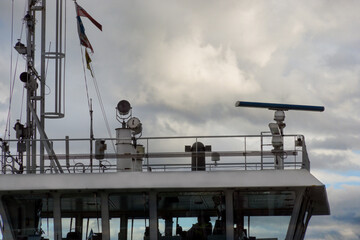 The upper deck, wheelhouse windows, and radar antenna mast of a modern vessel against a cloudy sky. Rotating Marine Radar, a horizontal antenna used for navigation and detecting obstacles.  © Jacek