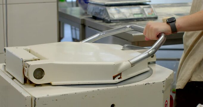 close-up of bakery dough press in commercial kitchen showing operator hands handling patterned dimpled dough on circular platen, white hinged lid is open revealing