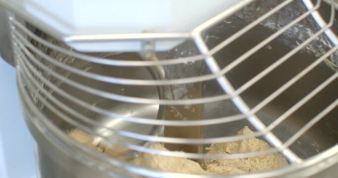 inside view of commercial planetary mixer showing dough being combined by central stainless paddle visible through curved wire safety guard, close elevated oblique