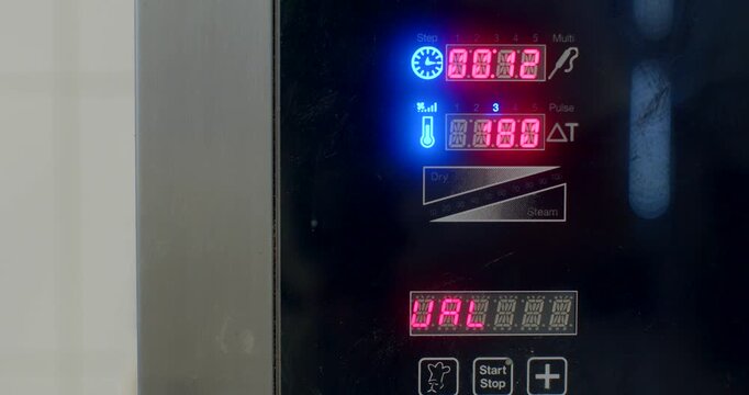 tight near-eye-level close-up showing microwave control panel illuminated by red seven-segment timers and blue status icons, lower display showing status letters
