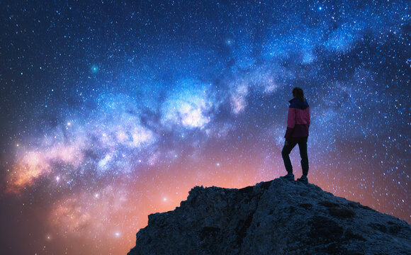 Glowing Milky Way and woman on mountain peak at starry night. Dolomites, Italy. Galaxy. Space landscape with silhouette of a girl, rocks, sky with bright stars. Milky Way and hiker. Nightscape