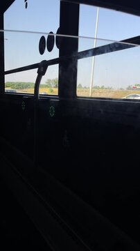 wheelchair priority area inside public bus shown from seated eye level, featuring vertical metal handrail and diagonal support bar beside side window, two