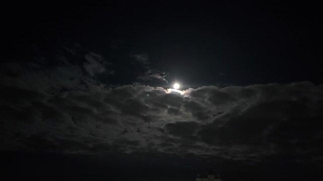 A black night sky covered with clouds, the moon.