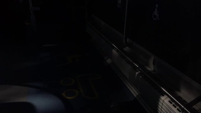 floor-level view along sidewall of public transport showing bright yellow wheelchair symbols painted on navy floor, metal handrails, foldable seat fittings, with