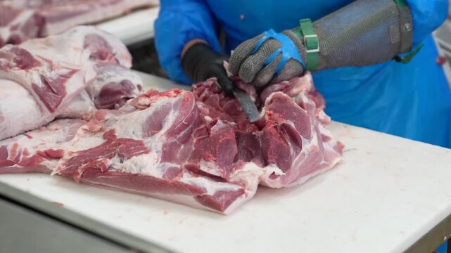 Worker using a knife to remove bones from a raw pork cut