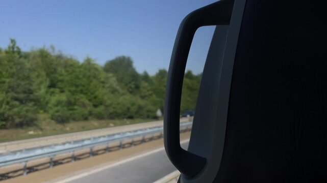 passenger side mirror housing stays sharp while outside highway scene streaks with blurred guardrail and truck sliding past under clear blue sunlit daytime sky
