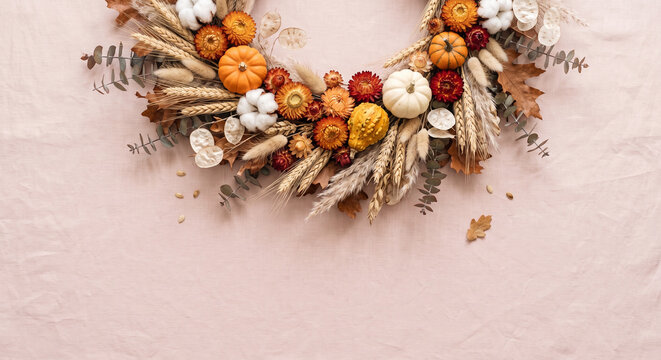 Boho autumn floral wreath with pumpkins and pampas grass on soft pink linen background.