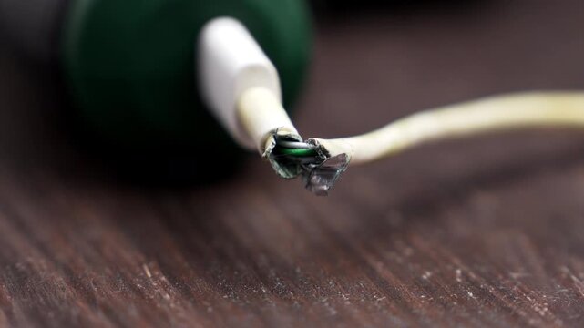 Broken charging wire with torn outer insulation plugged into a cordless screwdriver battery port on wooden table