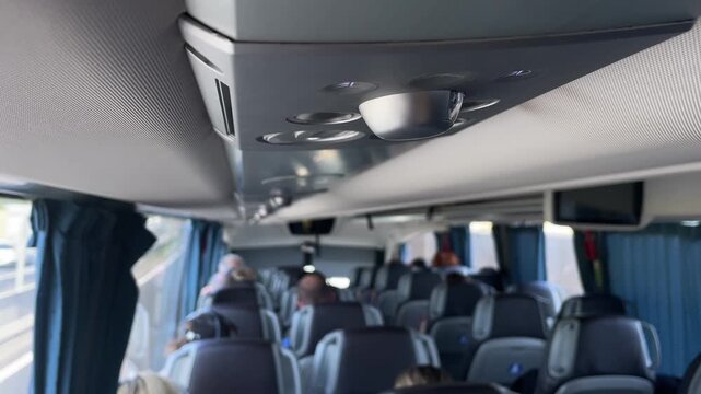 low-angle forward view along central aisle showing overhead panel with metallic reading light housing, circular air vents, and recessed controls while rows of vent