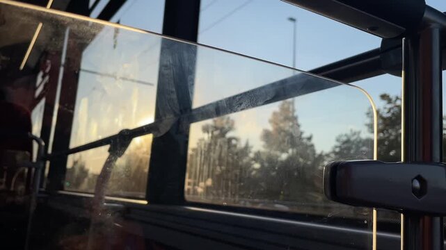 close-up of transparent bus divider with fingerprints, smudges, and scratches as warm sunset backlight shifts, creating moving rim highlights across metal support