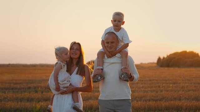 Happy young family with two small children enjoying a peaceful walk together through a golden field at sunset, sharing love, connection, and joyful moments outdoors