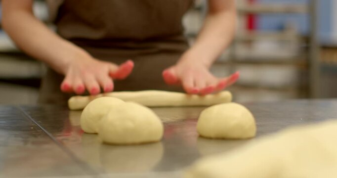 low-angle closeup of baker hands shaping raw dough balls on reflective stainless countertop in commercial bakery, warm even lighting highlights smooth glossy dough