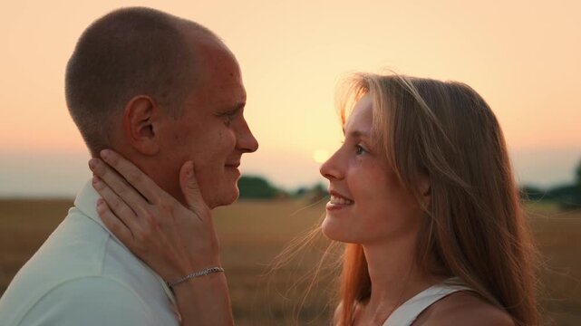 Romantic couple embracing in a peaceful golden field at sunset, sharing intimate eye contact and gentle touch in a warm summer evening atmosphere