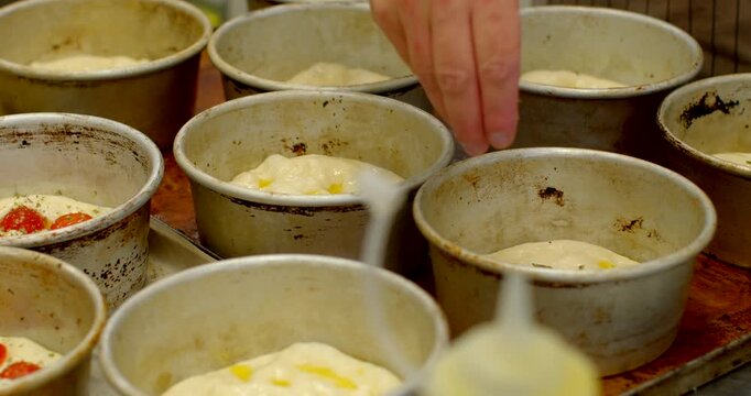 close-up view of baker placing raw dough portions into well used circular metal molds on baking tray, dough domes topped with olive oil and herbs in warm bakery