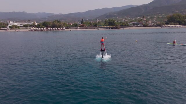 Woman Flyboarding with One Arm Raised Above the Sea, Takeoffs and Falls off Kalamata Beach, Greece, Drone View
