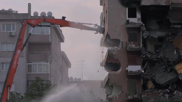Slow motion: demolition of building with water dust control, excavator with hydraulic crusher is tearing down the old typical Turkish multi-storey apartment, residential building in Istanbul, Turkey