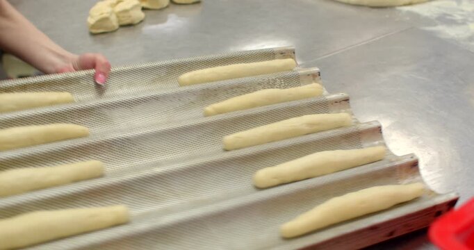 close-up motion of hands pressing and rolling small dough pieces on stainless steel bakery counter while rows of uniform dough logs rest on textured tray in, with