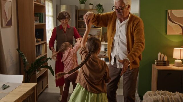 Senior Caucasian grandparents dancing and spinning young granddaughters at home. Clip fits commercials about retirement lifestyle, family insurance, pension funds and intergenerational connection