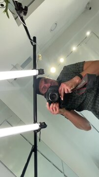 man leans over camera and adjusts settings with both hands while pointing finger near shutter in indoor studio, scene framed from extreme low upward viewpoint man