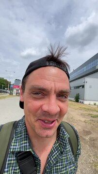 man smiling and looking at the camera, in outdoor possibly a park or open area with, with man, buildings, sky, from a close-up front-facing perspective perspective.