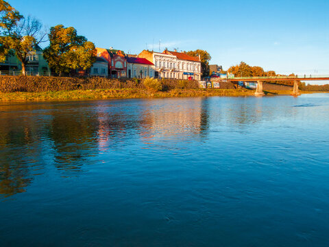 uzhhorod, ukraine - 30 aug, 2007: Uzh river in morning light. cityscape of the old european town reflecting in the water. grass embankment with trees and old architecture