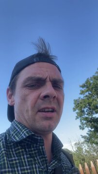 man speaking and looking around, in outdoors possibly in a park or open area, with man, sky, from a close-up focusing on the man's face perspective, nearby objects.