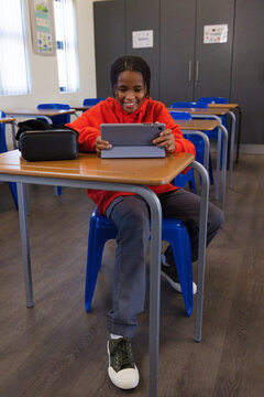 African American teen sitting at school desk in red hoodie smiling using tablet in gray folio