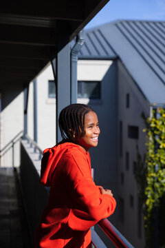 African American youth male wearing red hoodie leaning on balcony railing, smiling, looking right