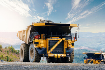 Massive yellow mining dump truck with gold ore in open pit quarry landscape for industrial banner background © Parilov