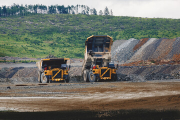 Two heavy dump trucks with ore in open quarry with green hillside for mining industrial site © Parilov