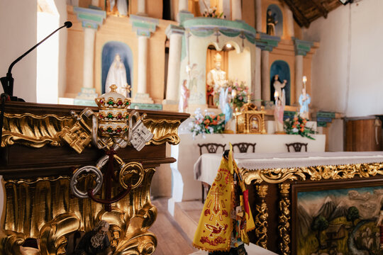 Ornate pulpit detail with gold religious symbols and microphone, blurred altar and statues of the virgin mary and saints in the historic iglesia de san pedro de atacama