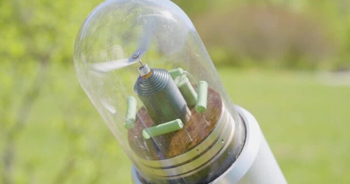 Close-up handheld shot of a small anemometer-like instrument at a weather station, its blade spinning rapidly under a glass dome and creating visible motion blur, accompanied by a whizzing sound. 