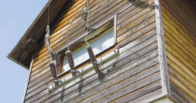 Low angle shot of electrical power line insulators connecting to an old wooden tower structure near weather station, showing weathered wood siding and ceramic insulator components