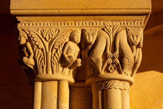 Detailed Romanesque carved stone capitals depict human figures and animal monsters illuminated by warm natural sunlight.