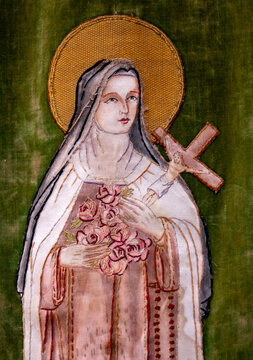 An embroidered religious textile depicts Saint Therese of Lisieux holding a crucifix and a bouquet of roses.