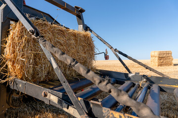 Farm equipment moves a hay bale on a sunny day in a field with other bales in the distance © Iryna