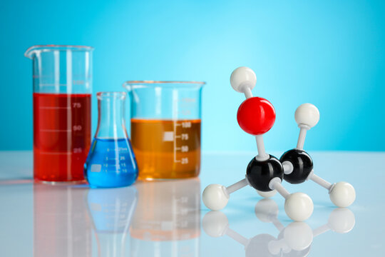 Chemical model of ethanol molecule and laboratory glassware on white table against light blue background, closeup