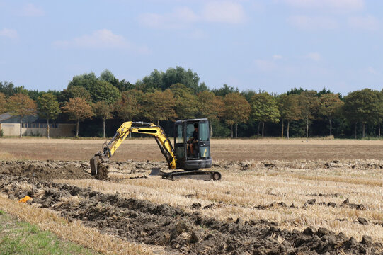 a little crane is digging trenches for installing drainage pipes in a field in summer
