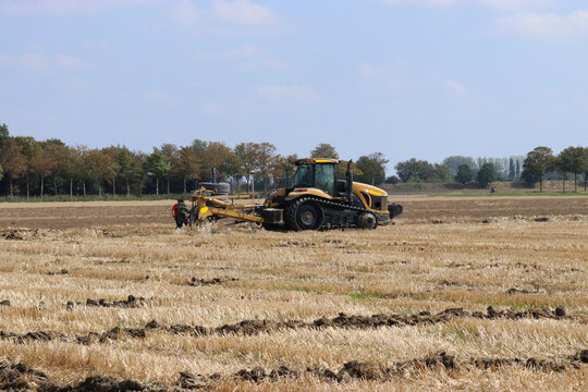 a farmer is with tractor with caterpillar tracks and a trenching machine installing drainage pipes in a field in summer after harvest