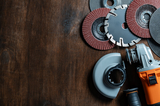 Electric angle grinder with an assortment of cutting, diamond, and flap sanding discs on dark wooden background, closeup. Perfect for hardware store promotions, construction and DIY workshop concepts